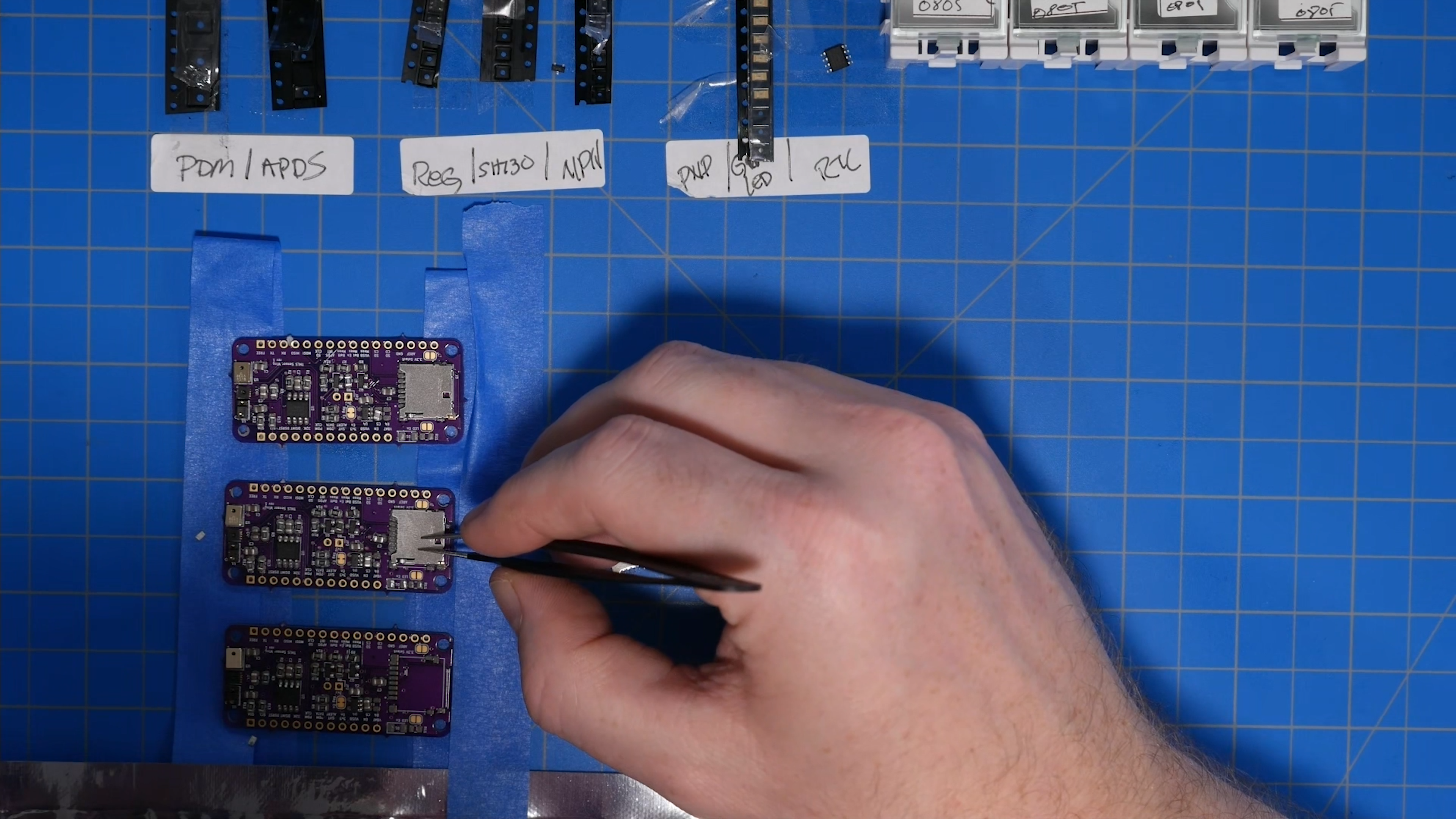 Three purple Bald SENSE sensor boards being assembled by hand on a work mat.